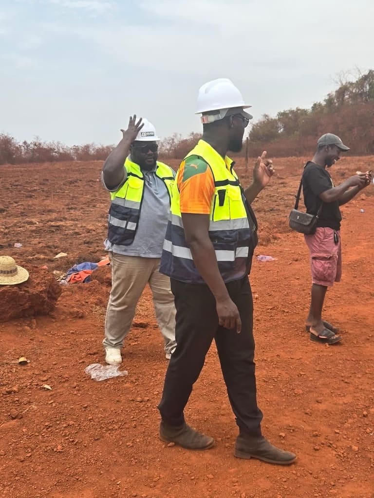 Petit groupe sur un site en terre rouge, un homme en casque blanc donne des indications