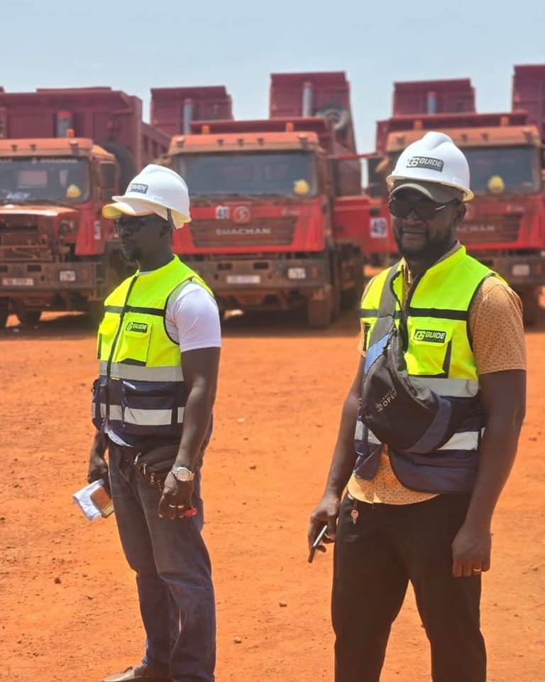 Deux superviseurs en casques blancs et gilets haute visibilité devant une rangée de camions-bennes